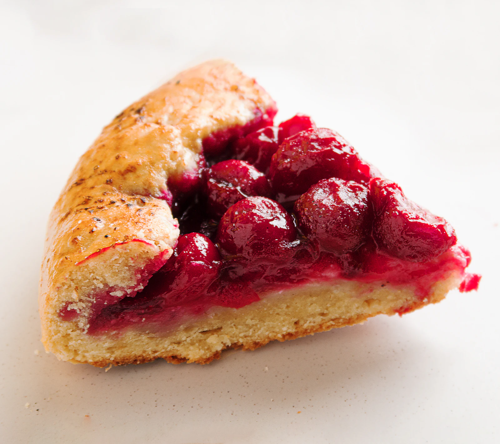 Holztisch mit Körben voller Rhabarber, Erdbeeren, Zwetschgen und Äpfeln vom Wochenmarkt, daneben eine frisch gebackene Beeren-Galette